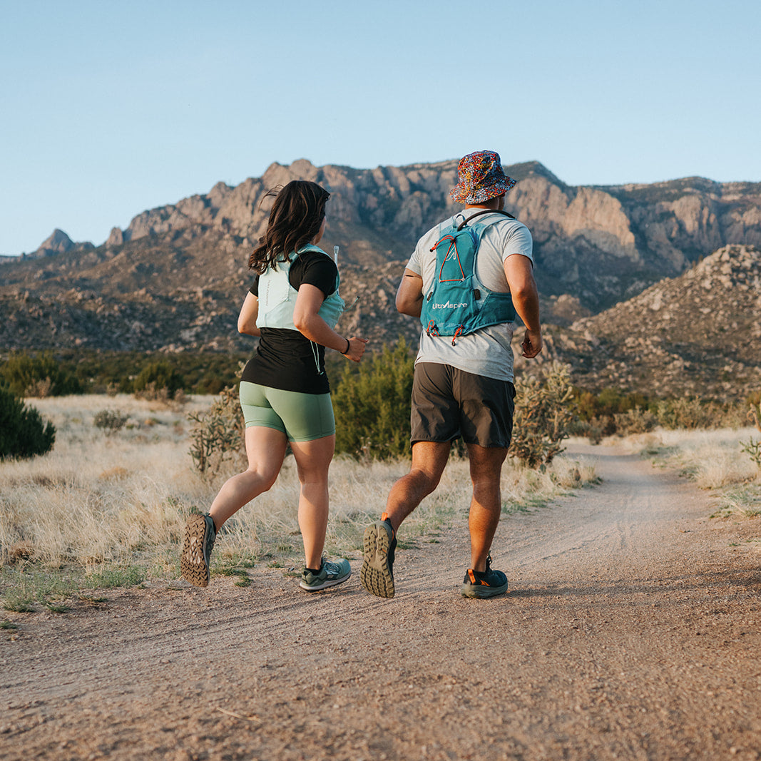 Two people running on a dirt road with mountains in the background